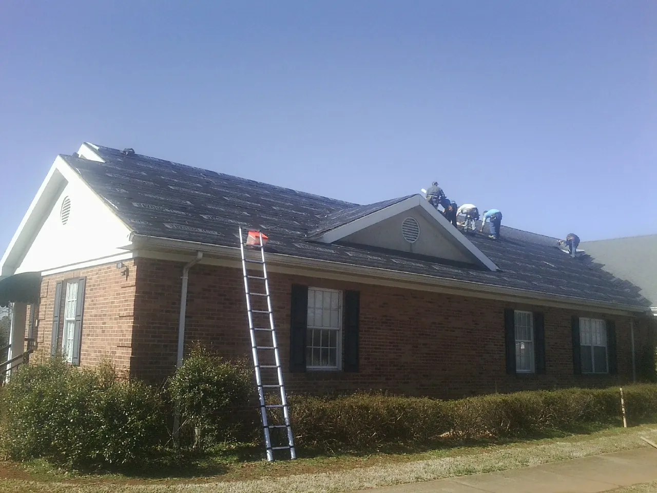 Crew tearing shingles off a brick ranch roof with a ladder set — Metal Roof Repair work by our crew in Basehor