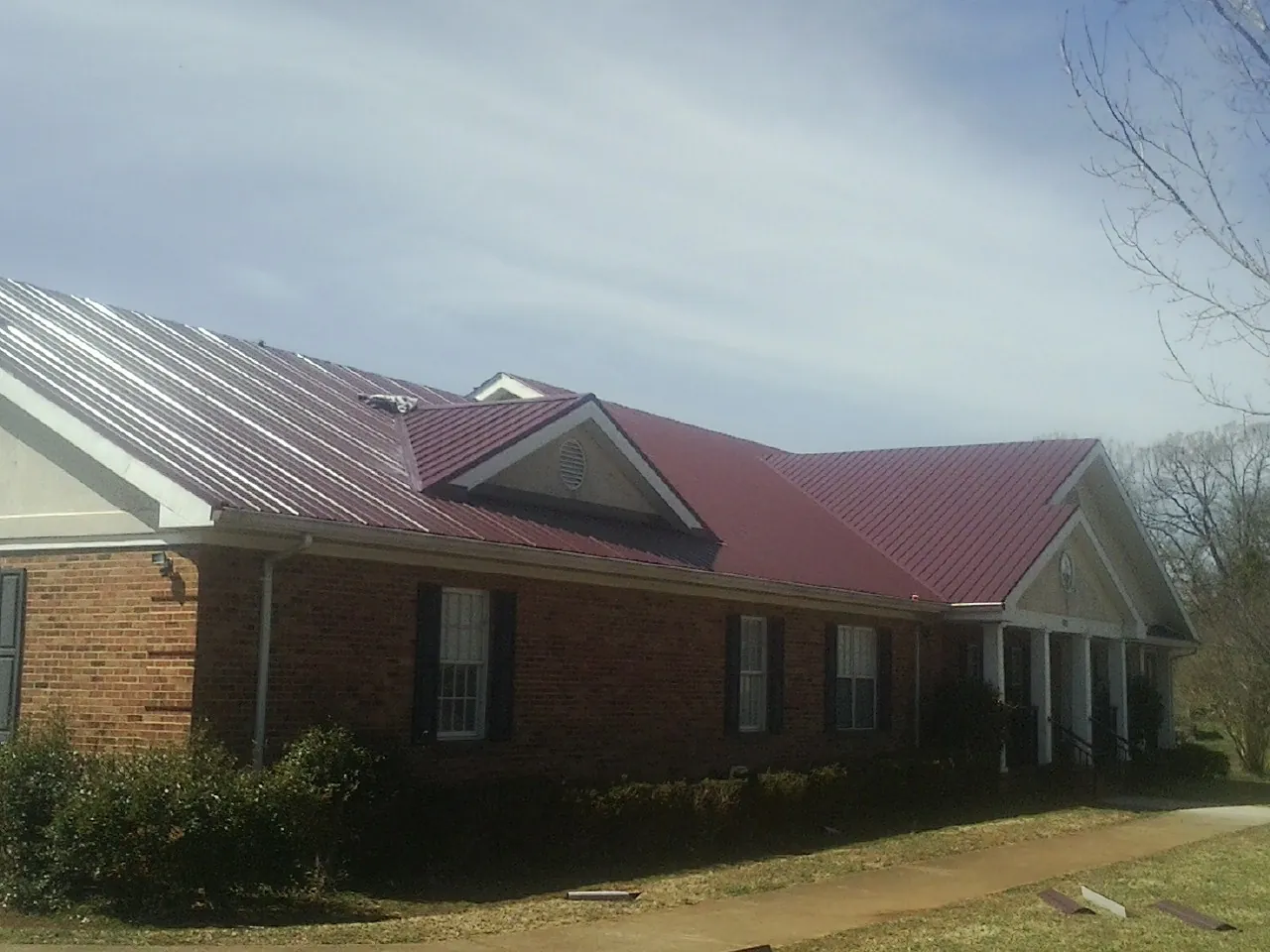 Red metal roof with gabled entries on a long brick building, from a Hail Damage Roof Repair job in Basehor