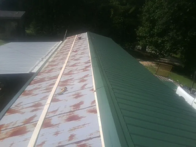 Old rusted panels beside newly installed green metal roofing — Wind Damage Roof Repair by Roofing Brothers in Basehor
