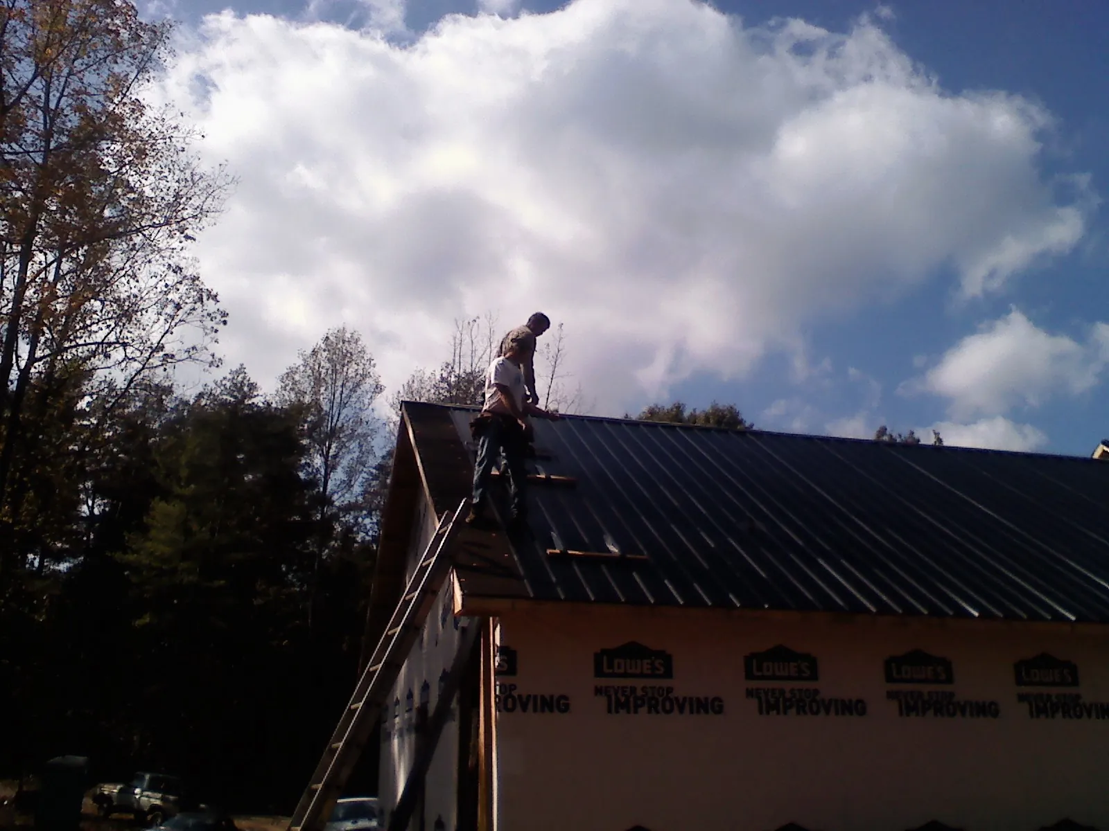 Roofer fastening dark metal panels high against a cloudy sky, from a Roof Inspection job in Basehor