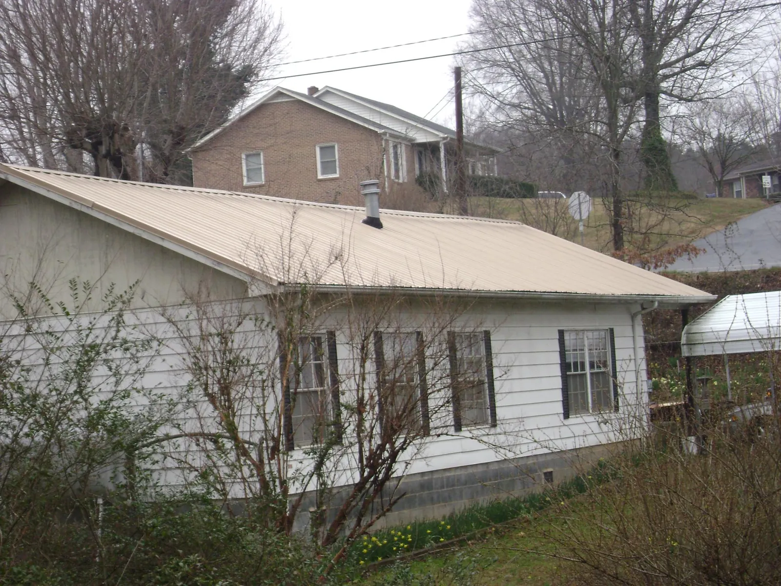 Tan metal roof on a white sided house set into a hillside — Commercial Roofing by Roofing Brothers in Basehor